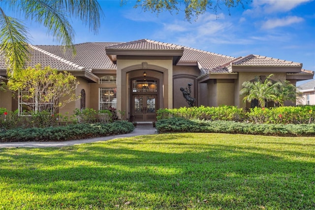 view of front facade featuring a front lawn, a tiled roof, french doors, and stucco siding