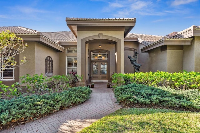 view of exterior entry with a tile roof, french doors, and stucco siding