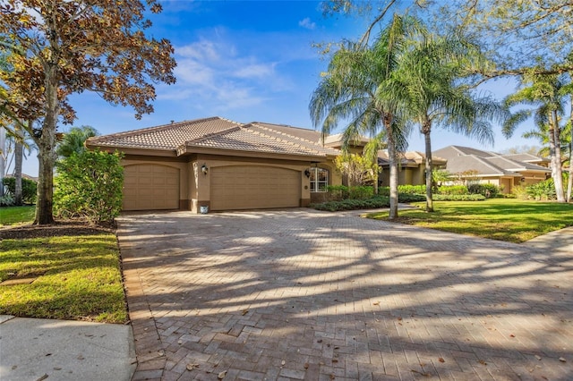 view of front of home with a front yard, an attached garage, stucco siding, a tiled roof, and decorative driveway