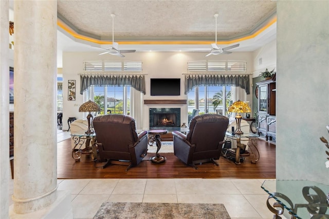 tiled living area featuring a lit fireplace, a raised ceiling, and ceiling fan