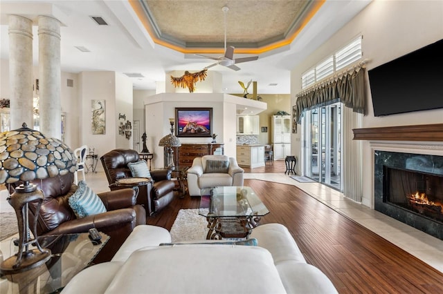 living area with a premium fireplace, visible vents, a raised ceiling, and hardwood / wood-style flooring