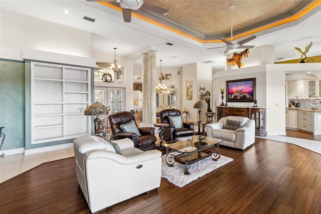 living area with hardwood / wood-style floors, a raised ceiling, ceiling fan with notable chandelier, and visible vents