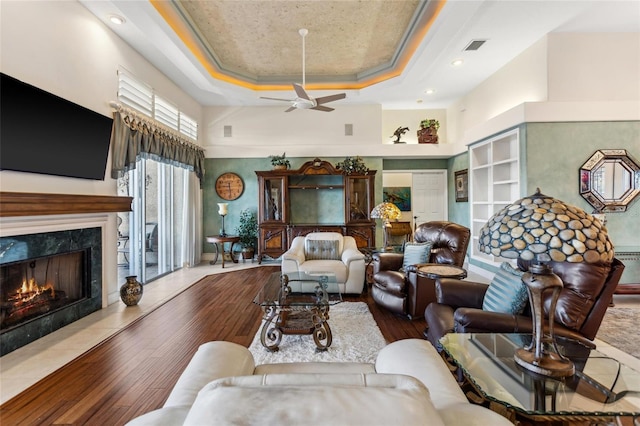 living room featuring crown molding, ceiling fan, a tray ceiling, a fireplace, and hardwood / wood-style flooring