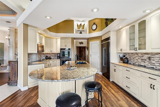 kitchen featuring an island with sink, a kitchen bar, light stone counters, black appliances, and a sink