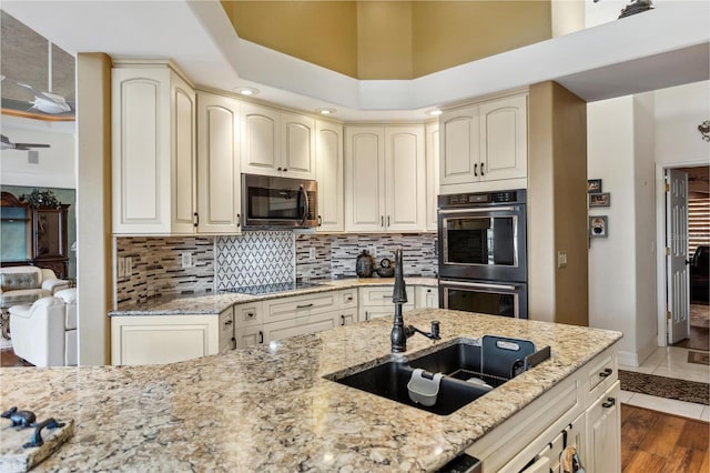 kitchen with stainless steel microwave, cream cabinetry, double wall oven, and black electric stovetop