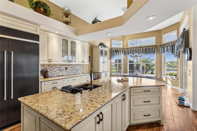 kitchen featuring wood finished floors, a sink, glass insert cabinets, high quality fridge, and tasteful backsplash