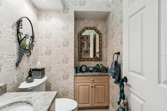 bathroom featuring toilet, wallpapered walls, and vanity