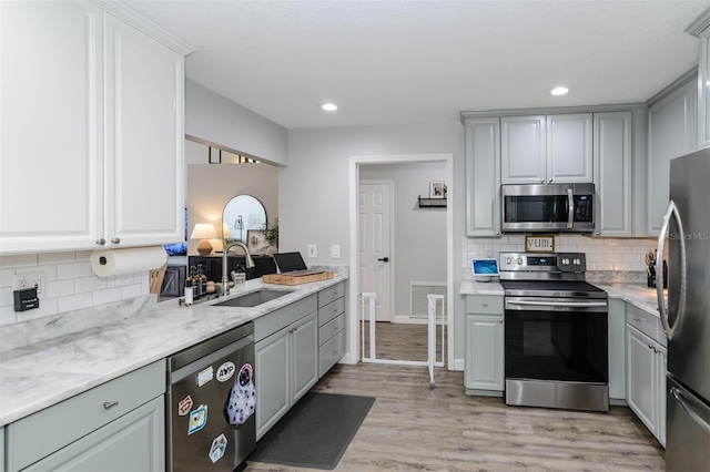 kitchen featuring gray cabinetry, a sink, appliances with stainless steel finishes, light wood finished floors, and decorative backsplash