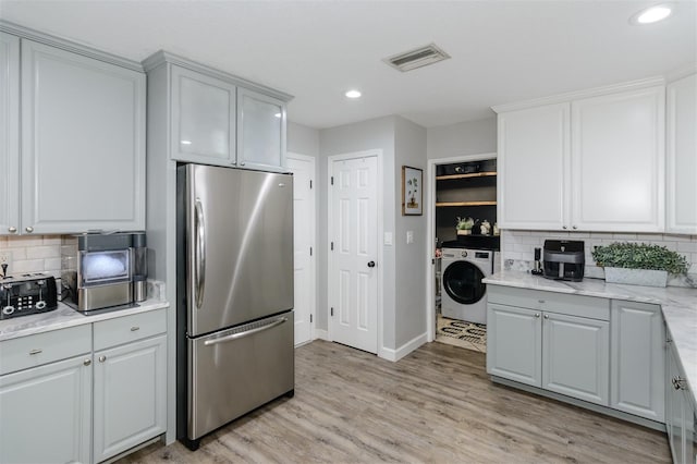 kitchen with visible vents, washer / dryer, freestanding refrigerator, light wood-type flooring, and backsplash