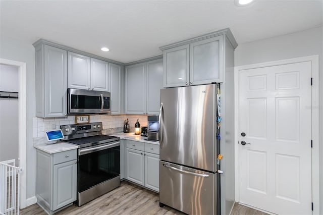 kitchen featuring gray cabinetry, light countertops, decorative backsplash, light wood-style flooring, and appliances with stainless steel finishes