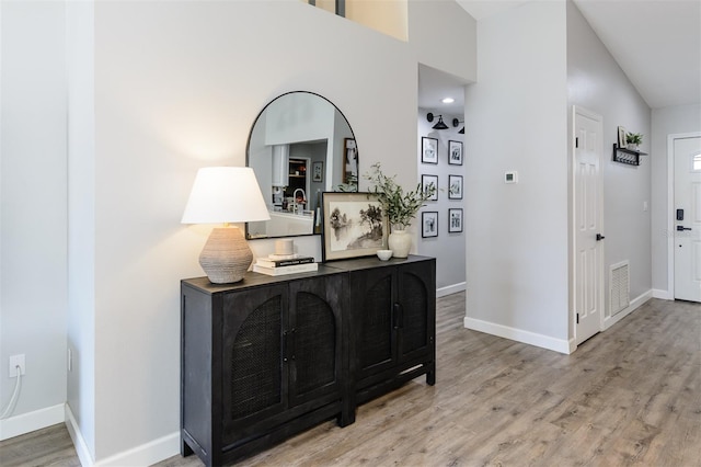 hallway with lofted ceiling, wood finished floors, visible vents, and baseboards