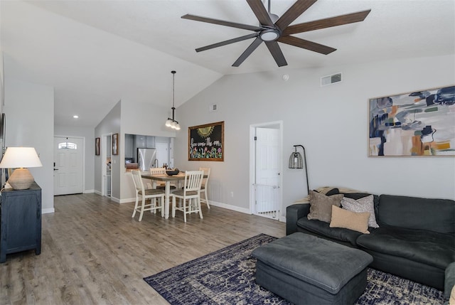 living room featuring visible vents, ceiling fan, baseboards, vaulted ceiling, and wood finished floors