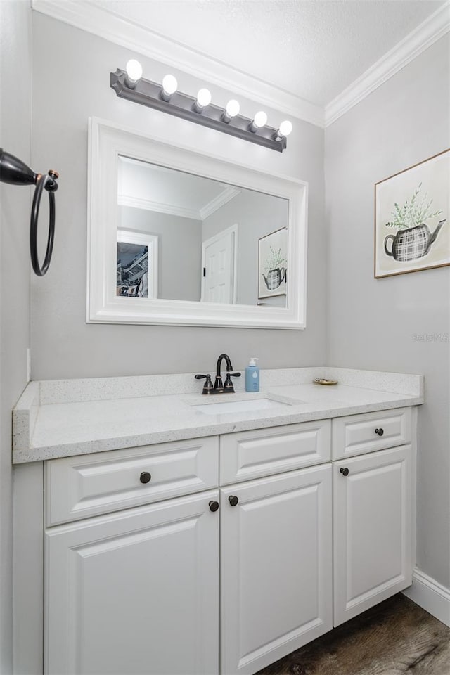 bathroom featuring baseboards, wood finished floors, ornamental molding, and vanity