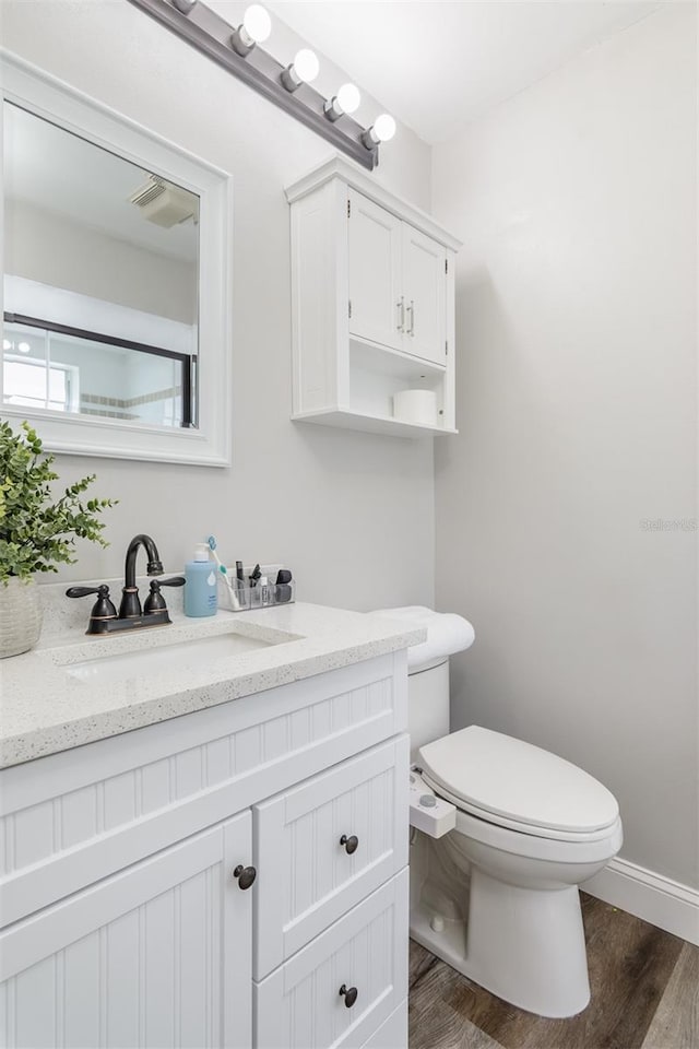 half bathroom with toilet, vanity, baseboards, and wood finished floors