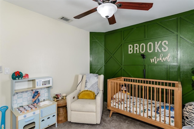 carpeted bedroom with visible vents, a nursery area, and a ceiling fan