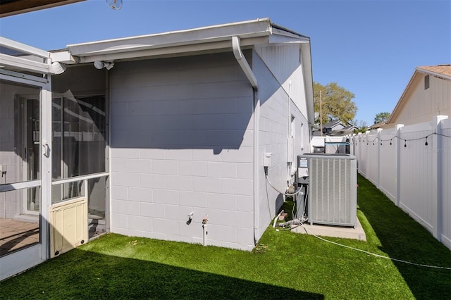 view of side of home featuring cooling unit, a yard, concrete block siding, and fence