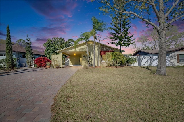 view of front of home with a carport, decorative driveway, a front lawn, and fence