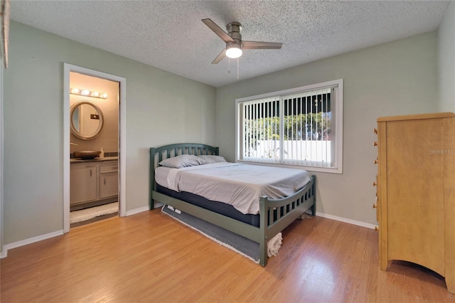 bedroom featuring wood finished floors, baseboards, ensuite bath, ceiling fan, and a textured ceiling