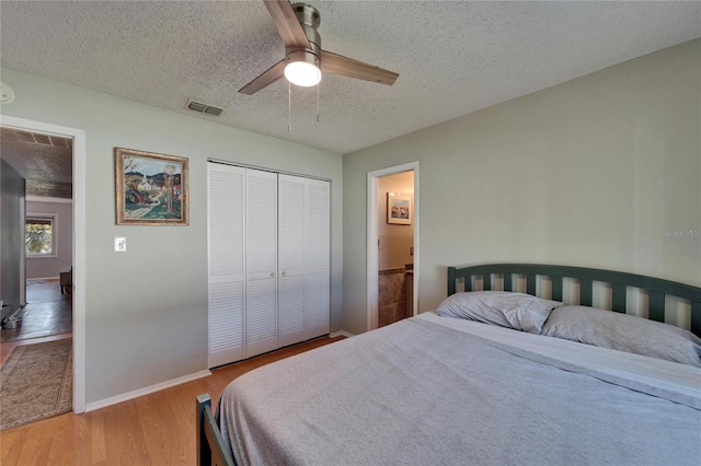 bedroom featuring wood finished floors, baseboards, visible vents, a closet, and a textured ceiling