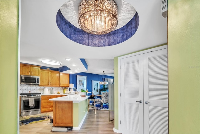 kitchen with a peninsula, appliances with stainless steel finishes, light countertops, decorative backsplash, and a chandelier