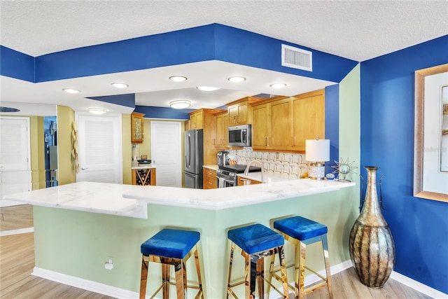 kitchen with a breakfast bar area, visible vents, a peninsula, light wood-style flooring, and stainless steel appliances