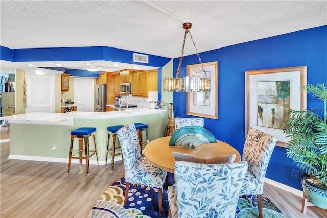 dining space featuring visible vents, baseboards, a textured ceiling, and light wood-style flooring