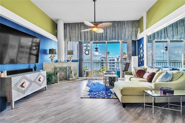 living area with ceiling fan, wood finished floors, a fireplace with raised hearth, and a towering ceiling