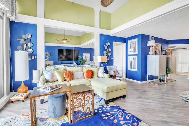 living area featuring visible vents, baseboards, ceiling fan, a towering ceiling, and wood finished floors