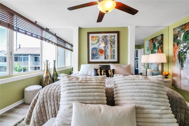 bedroom with a ceiling fan, wood finished floors, baseboards, and a textured ceiling