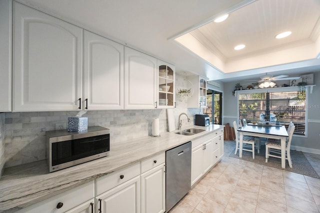 kitchen with a tray ceiling, a sink, stainless steel appliances, white cabinetry, and tasteful backsplash