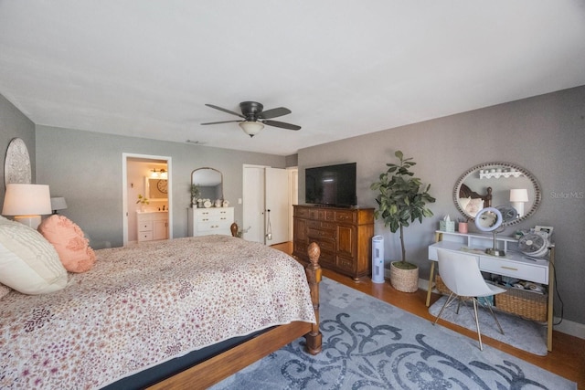 bedroom featuring wood finished floors, visible vents, baseboards, ensuite bath, and ceiling fan