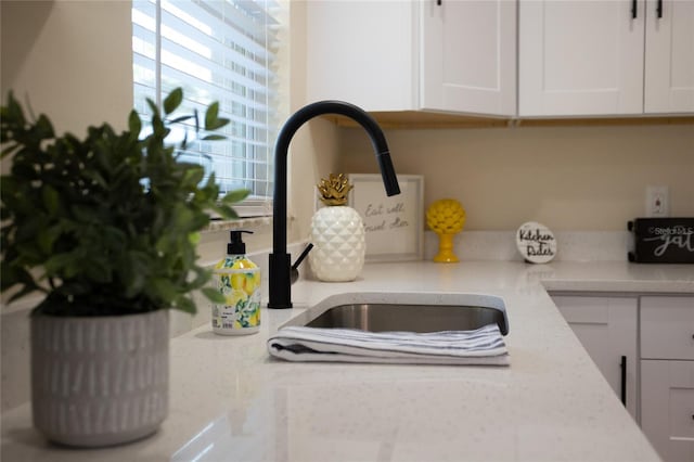 details featuring a sink, light stone counters, and white cabinets