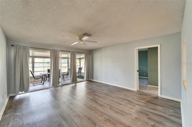 empty room featuring ceiling fan, visible vents, baseboards, and wood finished floors