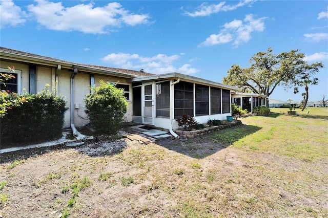 rear view of property featuring stucco siding, a yard, and a sunroom