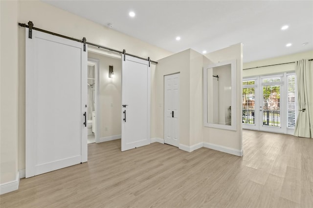 spare room with light wood finished floors, recessed lighting, baseboards, and a barn door