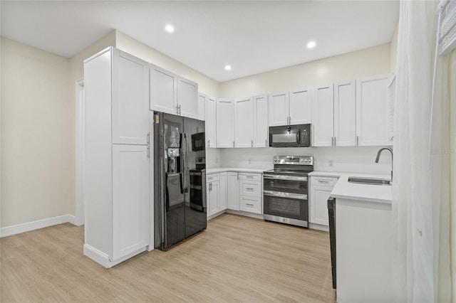 kitchen with a sink, black appliances, light wood-style flooring, and light countertops