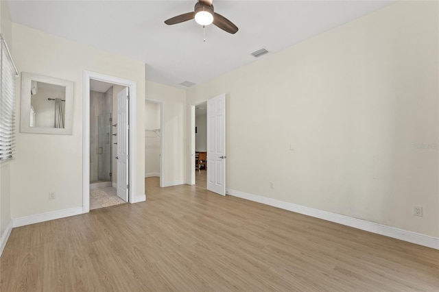 unfurnished bedroom featuring visible vents, baseboards, a walk in closet, and light wood-style floors