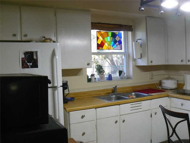 kitchen featuring a sink, freestanding refrigerator, light countertops, and white cabinetry