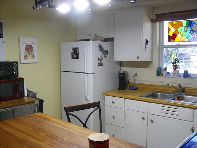 kitchen with white cabinets, freestanding refrigerator, and a sink