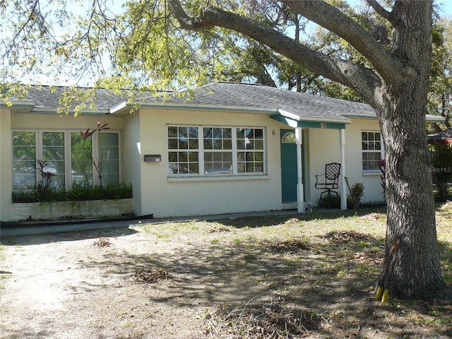 ranch-style home featuring stucco siding and roof with shingles