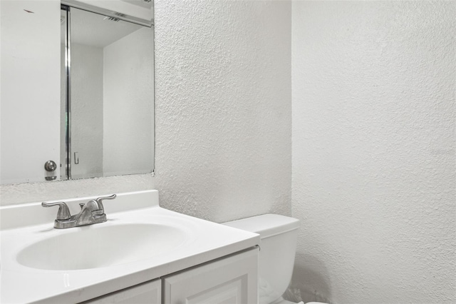 half bath featuring toilet, vanity, and a textured wall