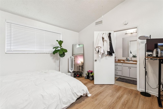 bedroom with visible vents, lofted ceiling, wood finished floors, a textured ceiling, and a sink