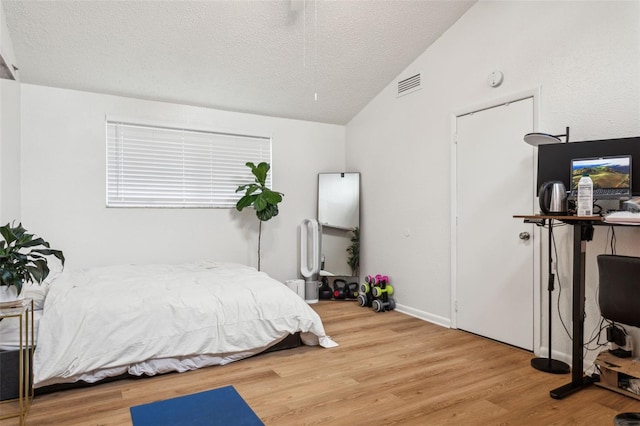 bedroom featuring lofted ceiling, wood finished floors, visible vents, and a textured ceiling