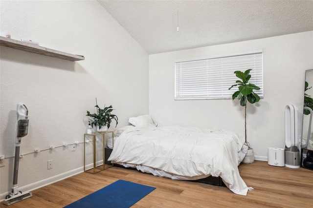 bedroom with a textured ceiling, lofted ceiling, baseboards, and wood finished floors