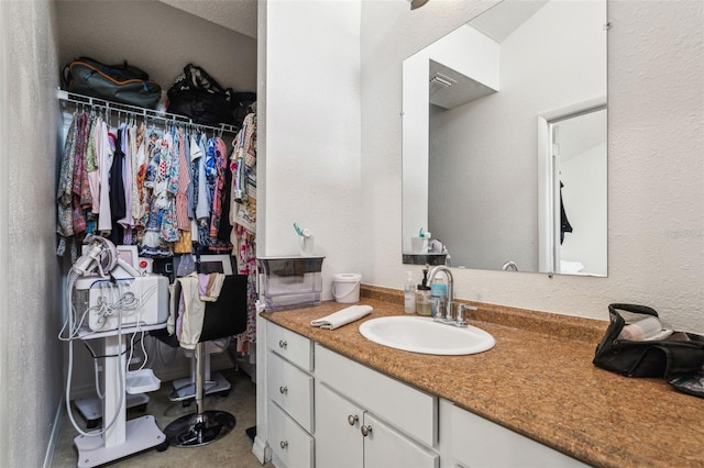 bathroom with vanity, a spacious closet, a textured wall, and visible vents