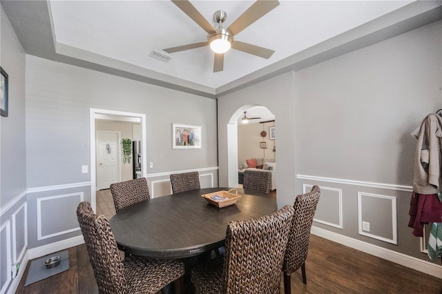 dining space with visible vents, wood finished floors, arched walkways, a decorative wall, and ceiling fan