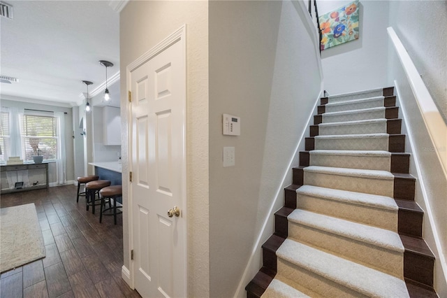 stairs with crown molding, wood finished floors, baseboards, and visible vents