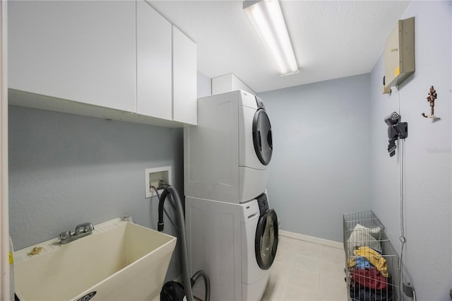 laundry area featuring stacked washer and dryer, a sink, electric panel, cabinet space, and baseboards