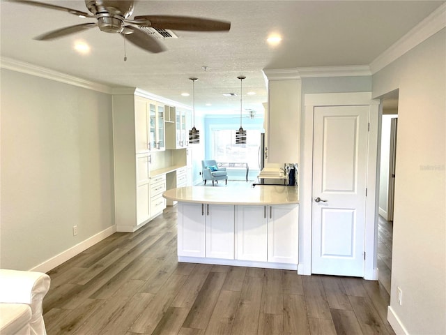 kitchen featuring a peninsula, wood finished floors, crown molding, and white cabinetry