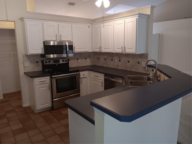 kitchen with a sink, dark countertops, white cabinetry, stainless steel appliances, and a peninsula